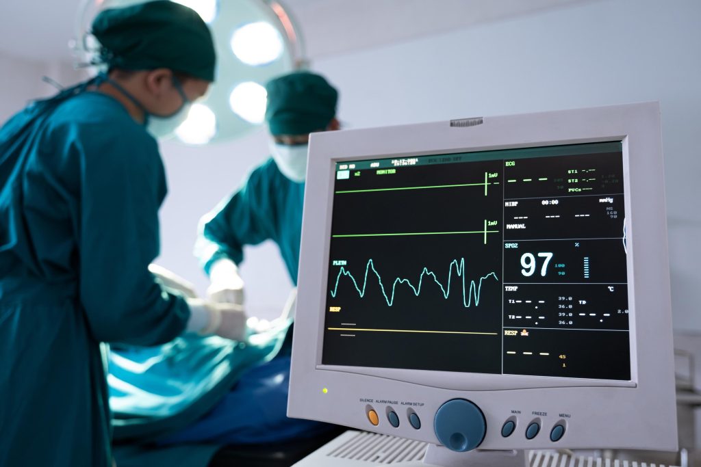Selective at monitor and nurse using defibrillator to pump at chest of unconscious with low heart rate patient to save life while doing medical surgery inside of operating room. Emergency CPR.